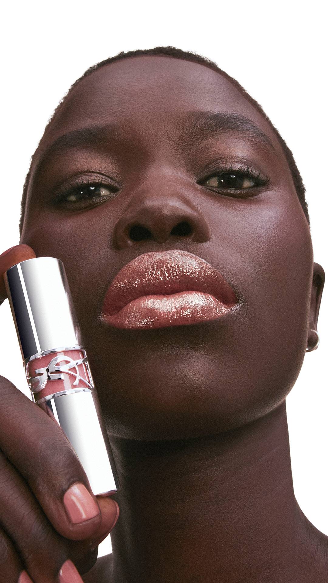 Mimi, dark skin, holds YSL LOVESHINE Lipstick shade 201 near her
glossy lips.