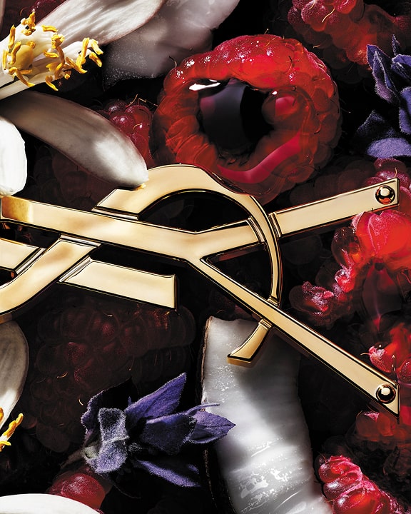 Close-up de framboesas e flores brancas com um detalhe dourado YSL Cassandre, evocando as notas florais frutadas de LIBRE Berry Crush.