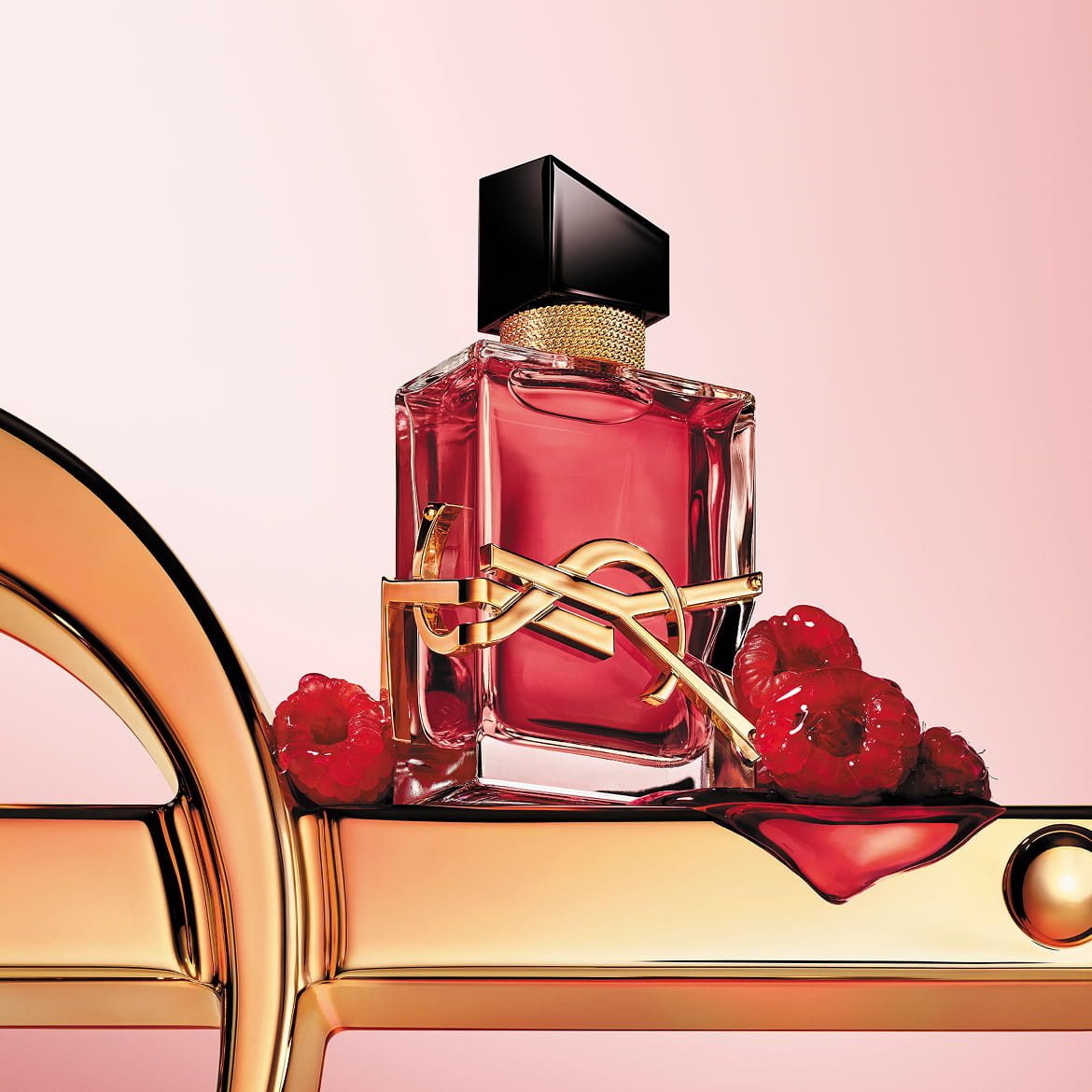 LIBRE Berry Crush berry-red perfume bottle with gold YSL Cassandre logo, styled with raspberries on a soft pink background.
