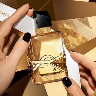 Libre eau de parfum perfume bottle with custom engraving, held by hands with black nail polish, on a golden background.
