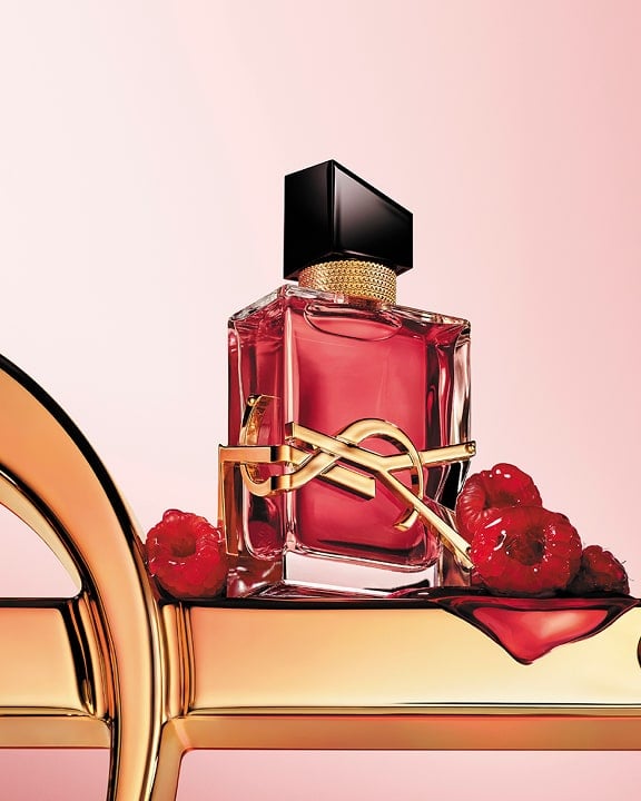 Frasco de perfume LIBRE Berry Crush vermelho-cereja com o logotipo dourado YSL Cassandre, decorado com framboesas sobre um fundo rosa suave.