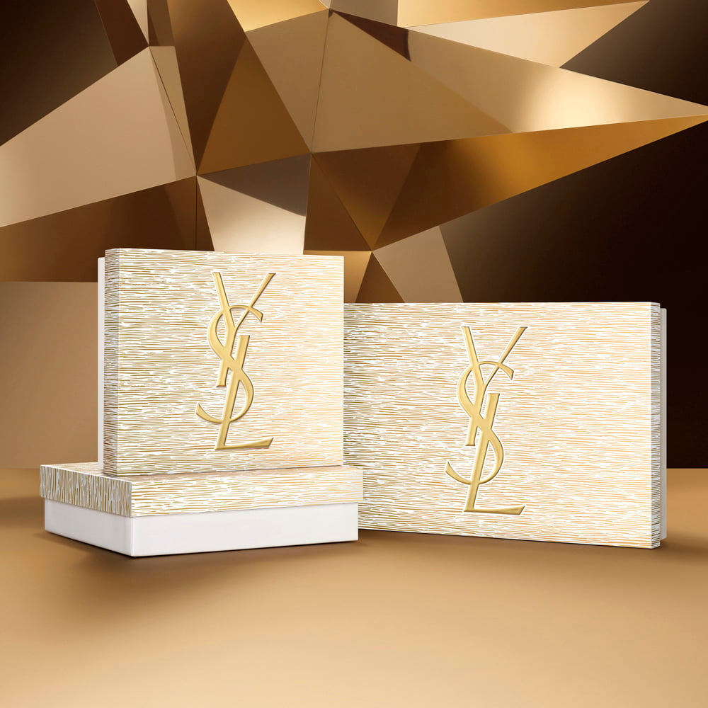 Holiday gift sets in gold tones with YSL Beauty logo, displayed on a geometric golden background.